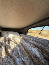 Comfy bed in an rv rental rooftop tent, featuring a floral duvet and panoramic desert views. Ideal for glamping adventures.