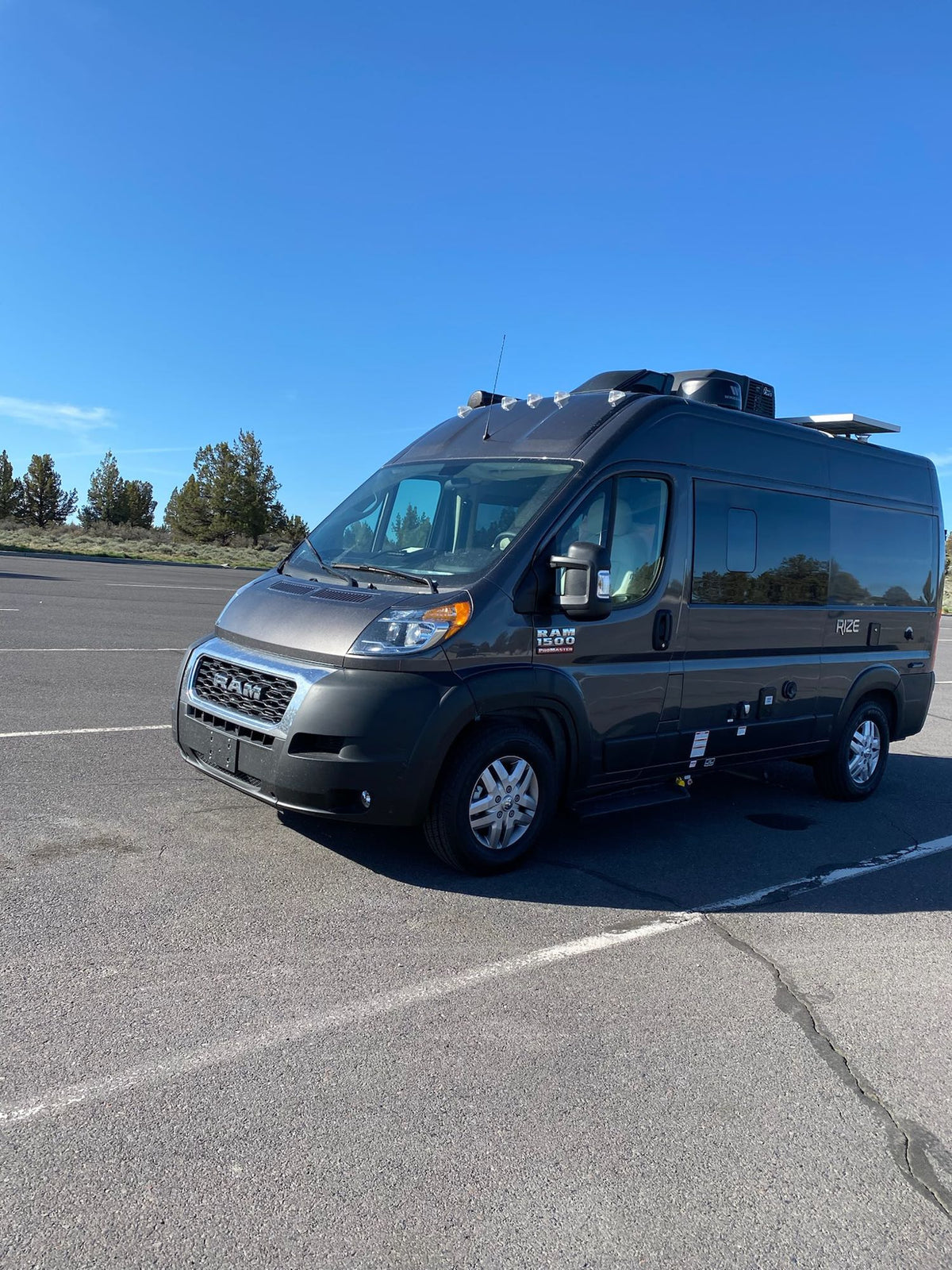  surrounded by tall trees.|An RV rental van parked among giant trees in a lush forest campsite with an extended awning.|Dark RV rental parked on a wet coastal road — photo 4