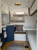 Inside a renovated RV rental. Features a full kitchen, comfortable bed, and dinette seating. Ready for your next adventure.