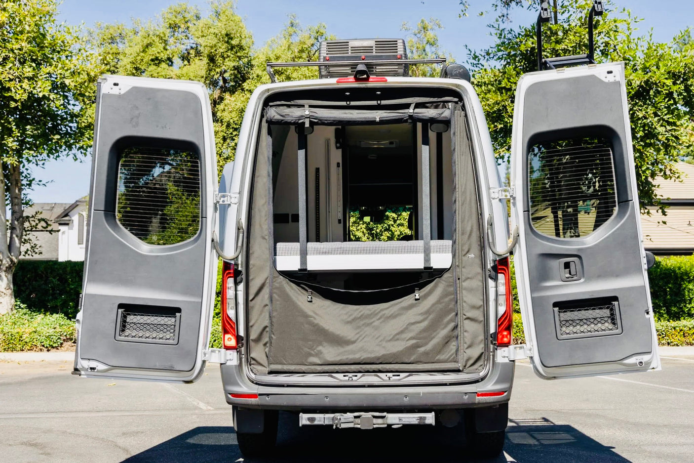Open rear doors of an RV rental van reveal a fabric interior enclosure, roof-mounted AC unit, and hitch receiver. Perfect for trips.