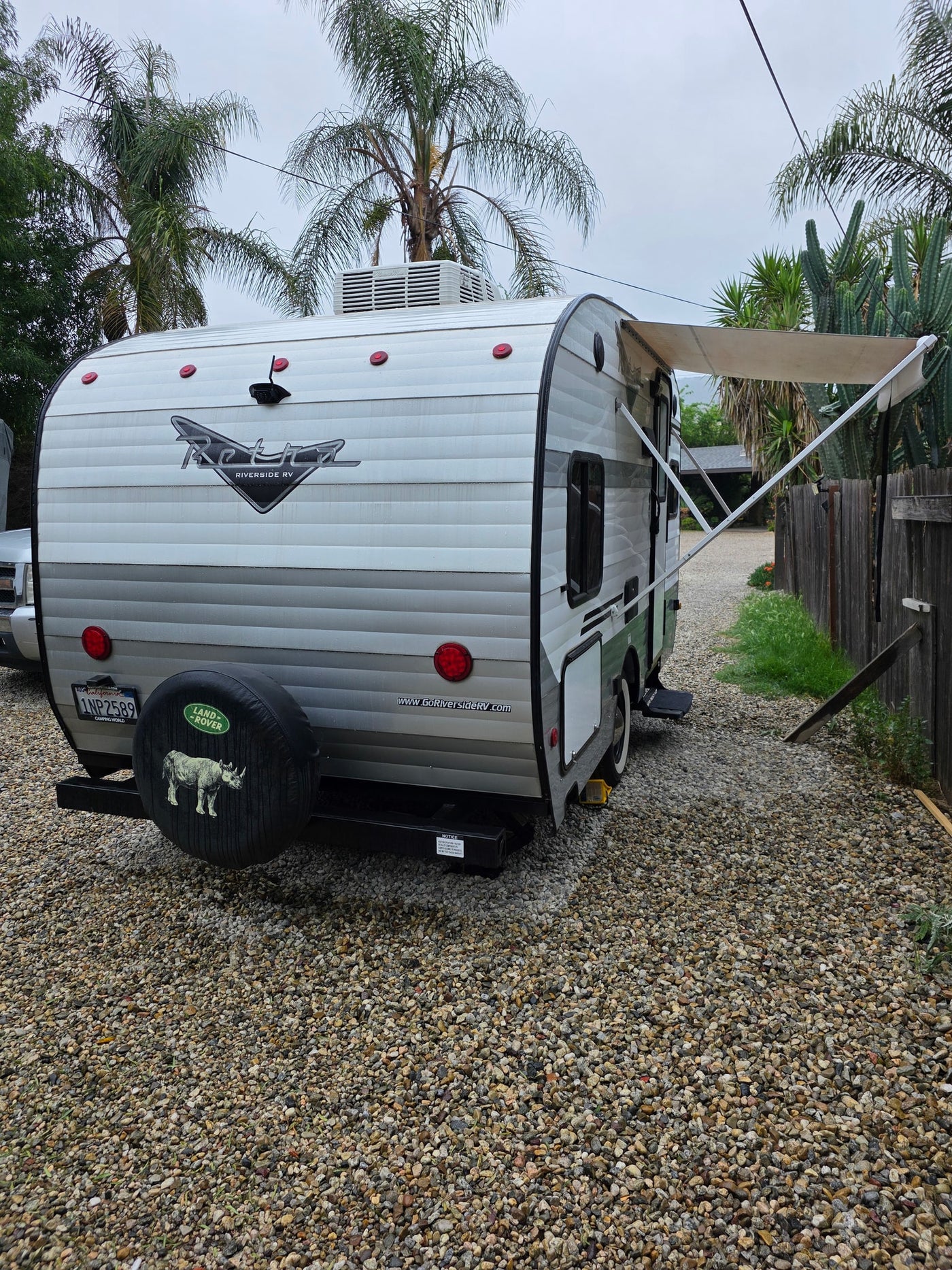 A retro-style travel trailer, a potential rv rental, is parked on gravel with its awning extended. Cloudy day. — photo 8