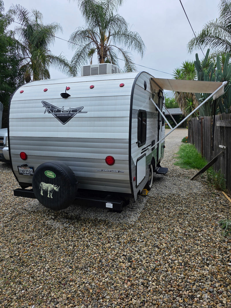 A retro-style travel trailer, a potential rv rental, is parked on gravel with its awning extended. Cloudy day. — photo 8