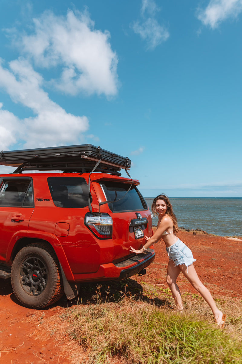 Red 4Runner SUV with an RV rental rooftop tent on a cliffside by the ocean. Woman smiles, ready for outdoor adventure. — photo 10