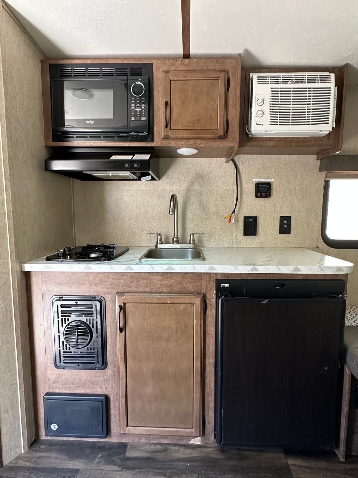 This RV rental kitchen features a microwave, stove, sink, fridge, and A/C, providing a full, compact setup. — photo 6