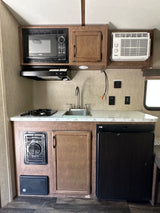 This RV rental kitchen features a microwave, stove, sink, fridge, and A/C, providing a full, compact setup.