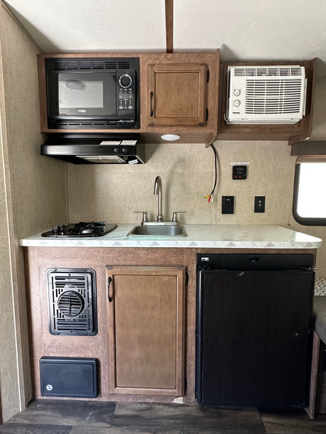 This RV rental kitchen features a microwave, stove, sink, fridge, and A/C, providing a full, compact setup.