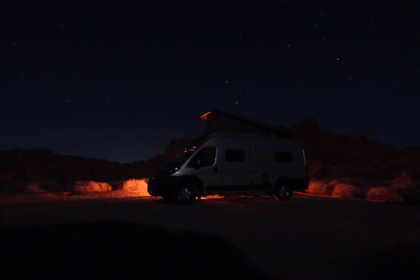 Night adventure! This rv rental camper van sits under a clear, starry sky, with warm lights illuminating the surrounding bushes.