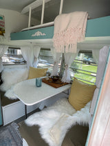 Charming RV rental interior with a cozy dining nook, teal bunk bed, and fluffy white throws, creating a bright and inviting space.