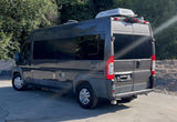 This dark grey camper van with a Dometic AC, seen from the rear 3/4 view, is an ideal RV rental.