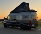 This dark gray Mercedes-Benz Sprinter camper van, featuring a pop-top, is ideal for an rv rental adventure at sunset.