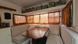 Cozy RV rental dining area: bench seats, a wooden table, plaid curtains, and overhead storage with baskets.