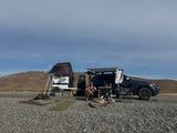 Overlanding adventure! A person relaxes with their SUV & trailer with a rooftop tent in a remote area. Great for an RV rental trip.