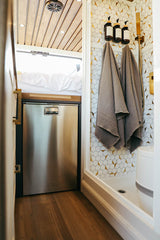 Sleek RV rental interior featuring a mosaic-tiled shower, stainless fridge, and cozy bed area.