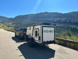 Truck tows a white camper trailer (RV rental) on a mountain road. Scenic outdoor adventure awaits under clear skies.
