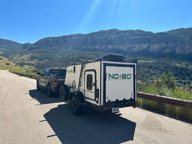 Truck tows a white camper trailer (RV rental) on a mountain road. Scenic outdoor adventure awaits under clear skies. — photo 17