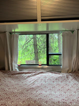 Inside a comfy RV rental bedroom: patterned bed, large window with forest views, and clear emergency exit signs.