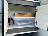Practical RV rental storage: an open cabinet reveals neatly stacked clear containers with towels, a wooden tray, and a gas cylinder.