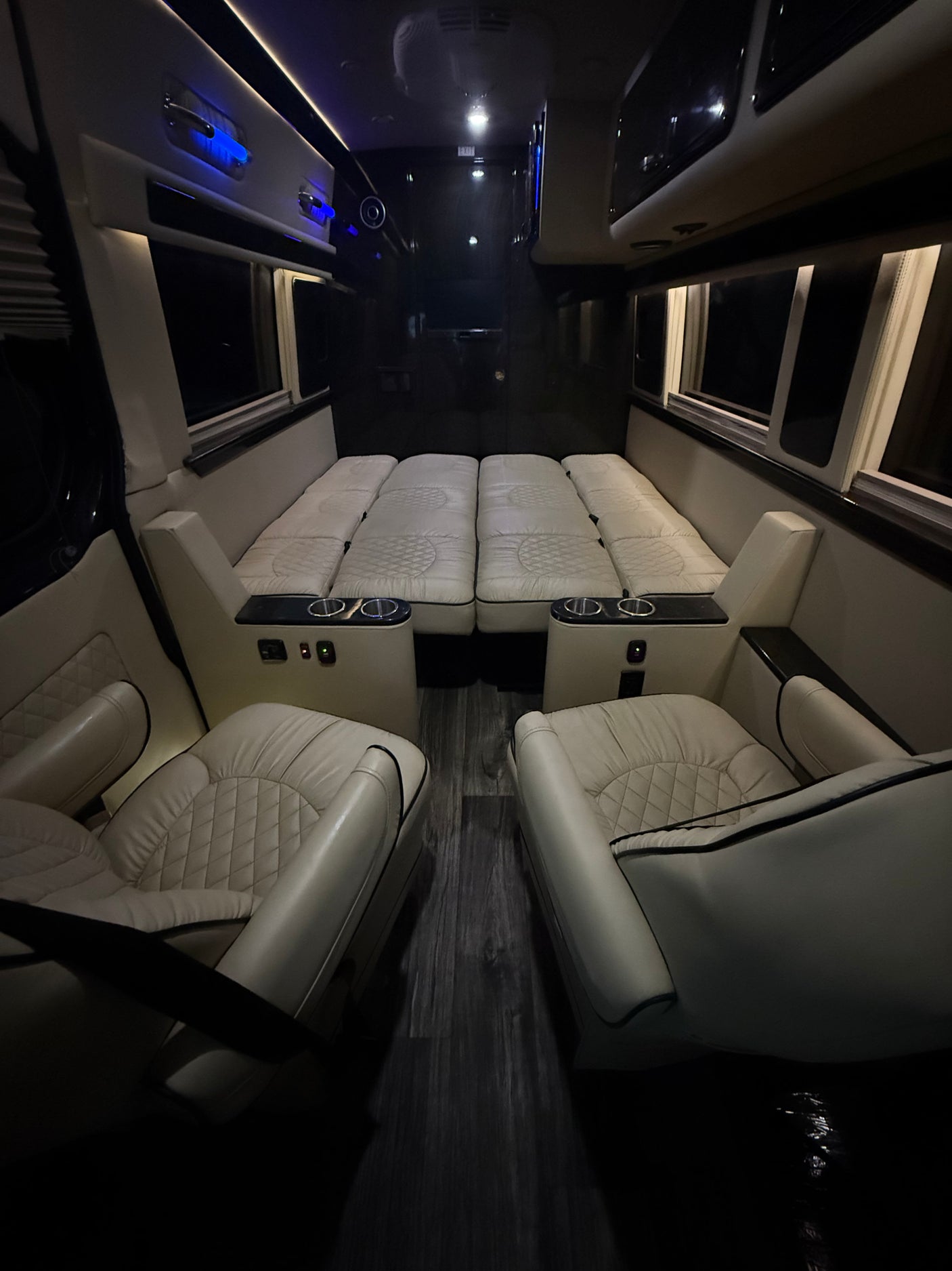 Premium RV rental interior features cream quilted seats, a fold-down bed, and dark wood flooring. Perfect for travel.