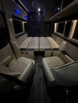 Premium RV rental interior features cream quilted seats, a fold-down bed, and dark wood flooring. Perfect for travel.