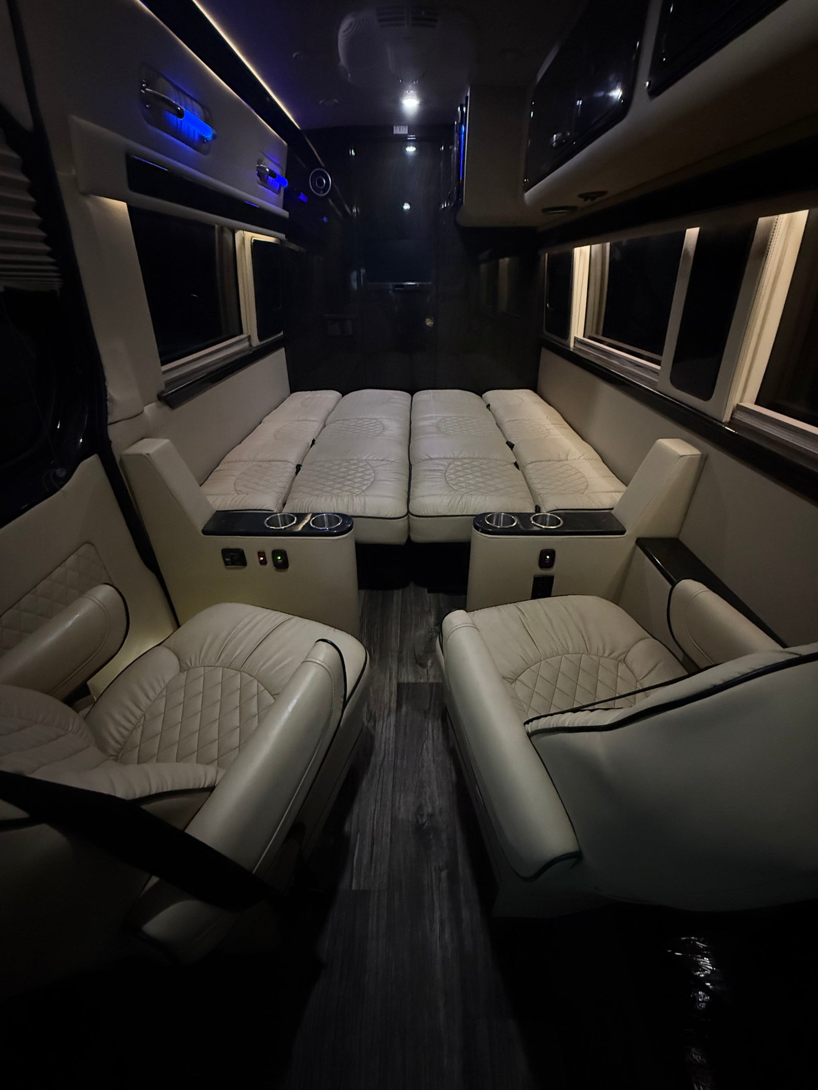 Premium RV rental interior features cream quilted seats, a fold-down bed, and dark wood flooring. Perfect for travel.