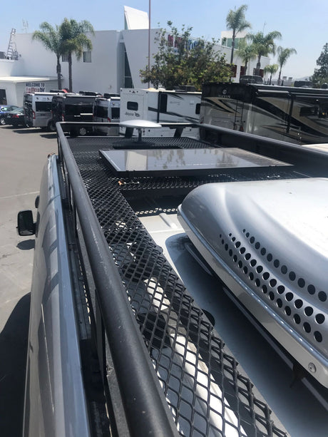 Rooftop view: solar panels, AC unit on an RV. Behind it, a sunny rv rental lot with diverse vans & motorhomes.