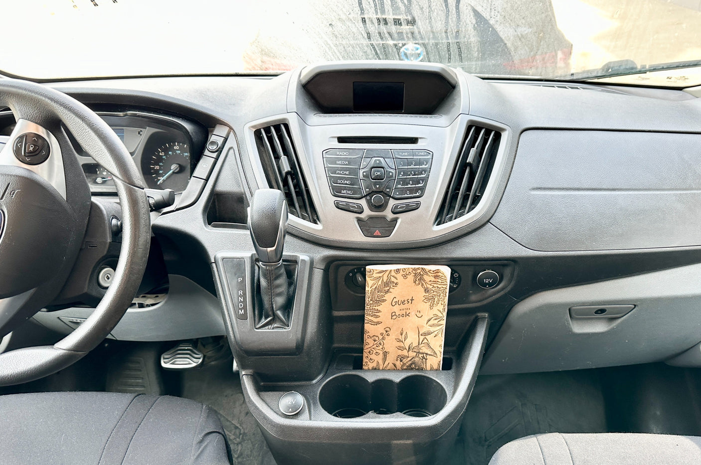 Dashboard view of an RV rental, showing the steering wheel, console, and a "Guest Book" in the cup holders.