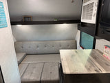 Cozy RV rental interior featuring a gray sofa-dinette, light wood-look countertop, and an AC unit for comfortable travel.