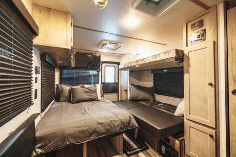 This RV rental showcases a cozy interior featuring a queen bed, overhead bunk, mounted TV, and ample storage cabinets.
