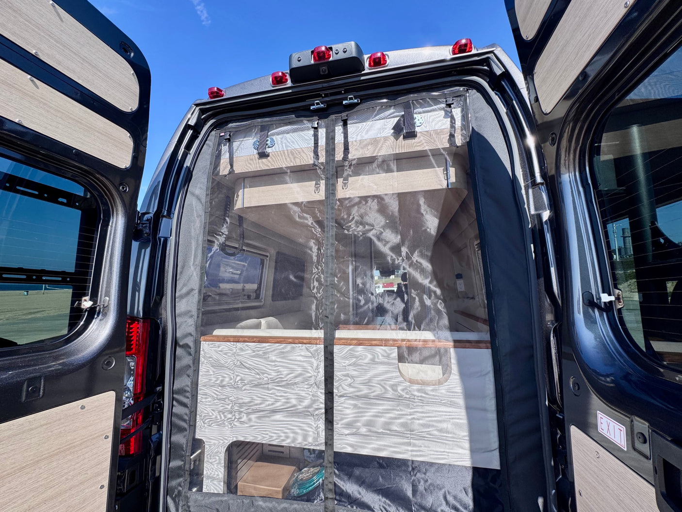 Rear view of an **RV rental** camper van with open doors, revealing a screen and the interior bed/living space.