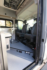 View into an rv rental camper van, showing the front seats, dinette table, and gray textured floor.