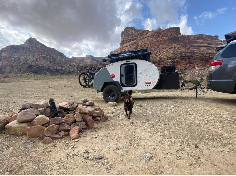 Experience outdoor adventure with an RV rental: a teardrop camper parked in a desert landscape with a dog and campfire. — photo 3