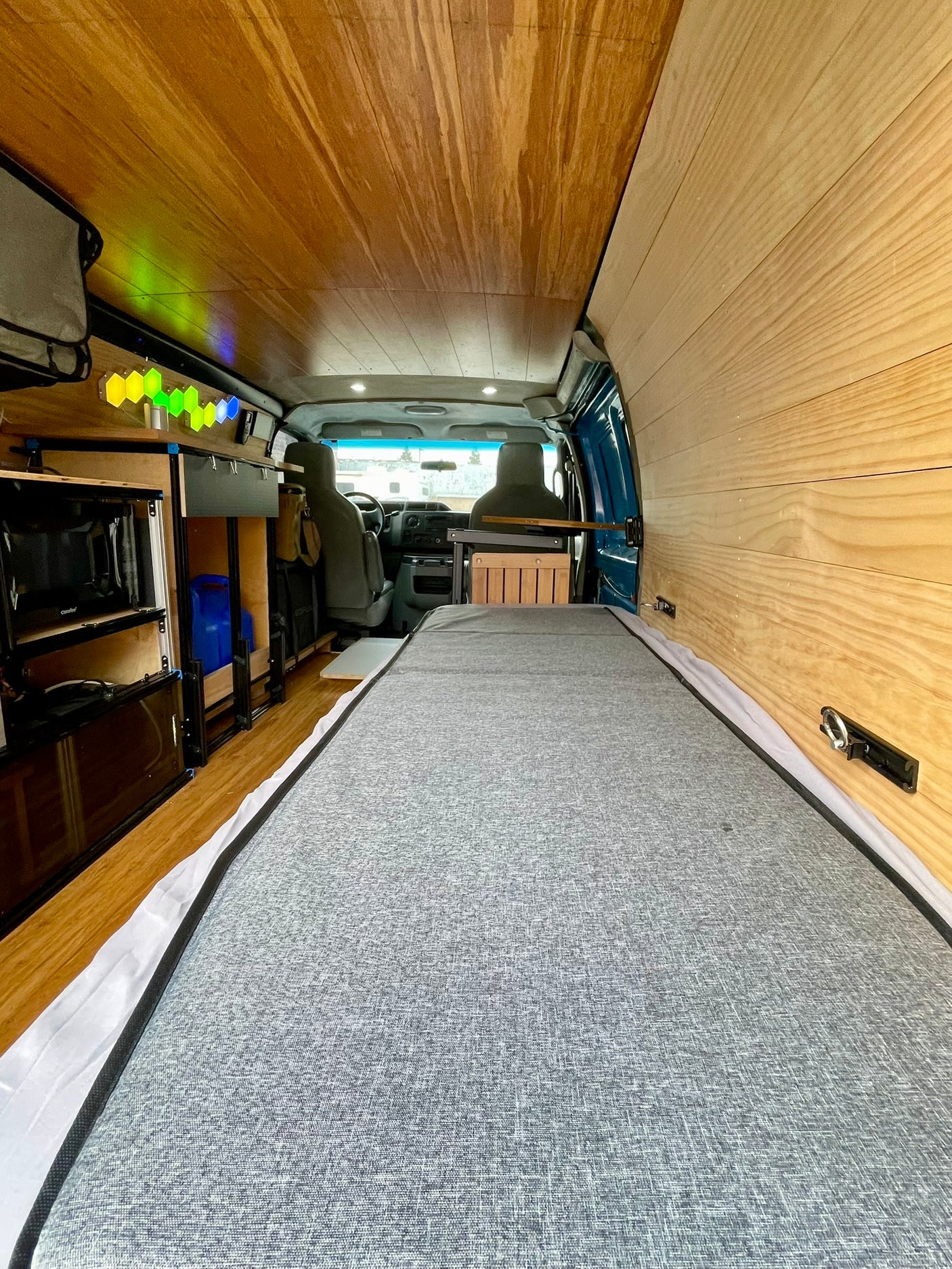 RV rental interior showing a bed, wooden walls/ceiling, kitchen area with appliances, and vibrant hexagonal lights.