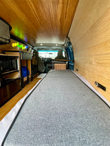 RV rental interior showing a bed, wooden walls/ceiling, kitchen area with appliances, and vibrant hexagonal lights.