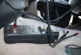 Black Duracell power strip/inverter with USB and AC outlets on an rv rental floor, powering various devices.