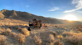 Enjoying a desert sunset in an RV rental. A person relaxes outside their camper van with an awning, surrounded by mountains.