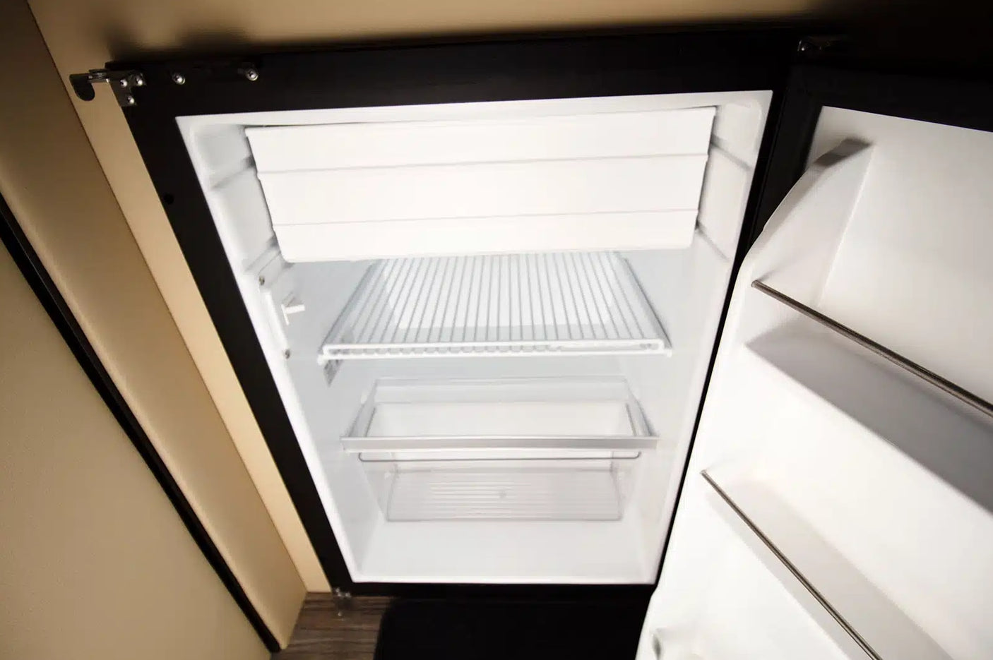 Inside a clean, empty compact refrigerator in an RV rental, featuring a freezer, wire shelf, and clear drawer.