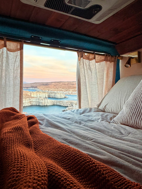 Relax in this cozy RV rental bed, offering expansive views of a lake nestled within rocky canyons at sunrise/sunset.