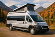White pop-top camper van for RV rental parked by a serene lake with autumn trees and mountains.|Enjoy nature with this RV rental! A silver camper van with an awning and chairs is parked on green grass under blue skies.|An rv rental camper van with pop-top and awning is set up on a grassy field. A smoking grill and distant mountains complete the scene.|Waterfront RV rental