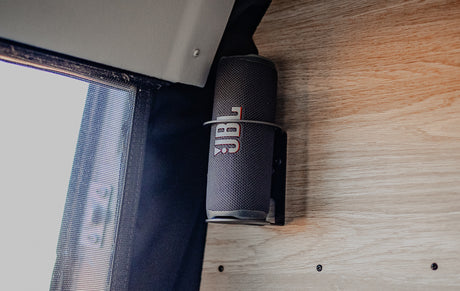 JBL portable speaker in a custom mount on wood panel, next to a window screen in an RV rental for easy tunes.