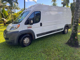 This white Ram ProMaster 2500 van, perfect for an RV rental, is shown parked on vibrant green grass amidst tropical palm trees.