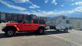 An orange Jeep Rubicon tows a Freesolo teardrop RV rental in a sunny parking lot, ready for travel.