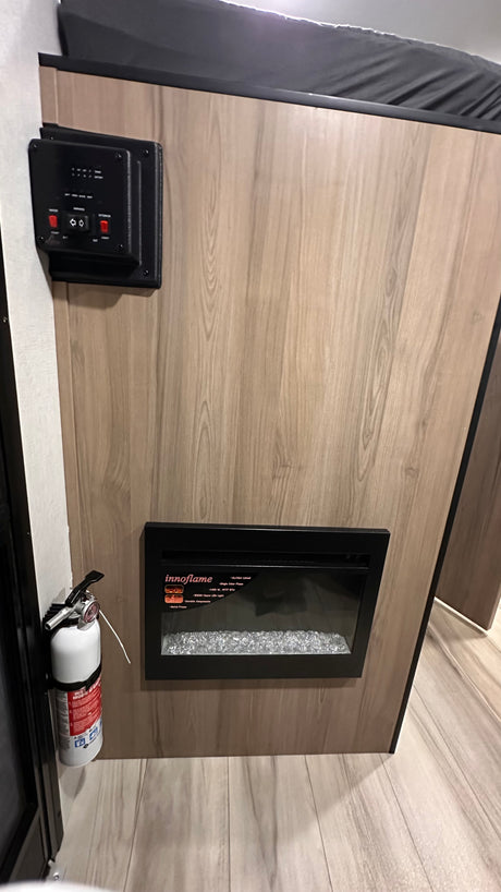 An RV rental's interior wall features essential controls, an Innoflame electric fireplace, and a fire extinguisher for safety.