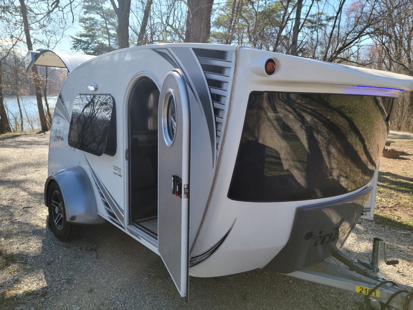Compact white & gray teardrop RV rental parked by a lake, ready for camping and outdoor adventures.