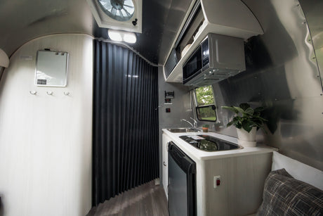 Inside a modern RV rental: a compact kitchen with microwave, sink, stovetop, and fridge, plus a flexible room divider.