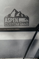 Aspen Custom Vans logo on a dark gray textured vehicle surface, featuring mountains & a camper van; great for rv rental.