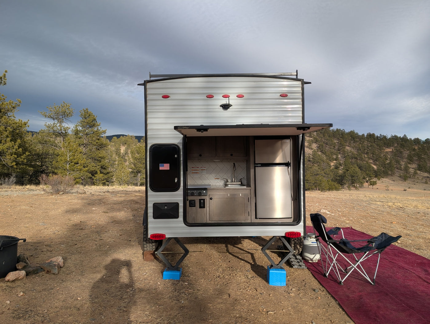 RV rental with an open outdoor kitchen, set up in a natural landscape with pine trees and mountains under a cloudy sky. — photo 4