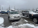 Snowy winter parking lot with cars, trucks, and an RV rental. Snow-covered trees under an overcast sky.