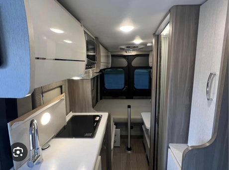 Efficient RV rental interior: modern kitchen with sink/stove, overhead cabinets, and rear bed/seating area.