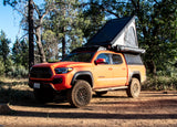 Orange Toyota Tacoma pickup truck with rooftop tent, ready for an RV rental camping adventure in the forest.