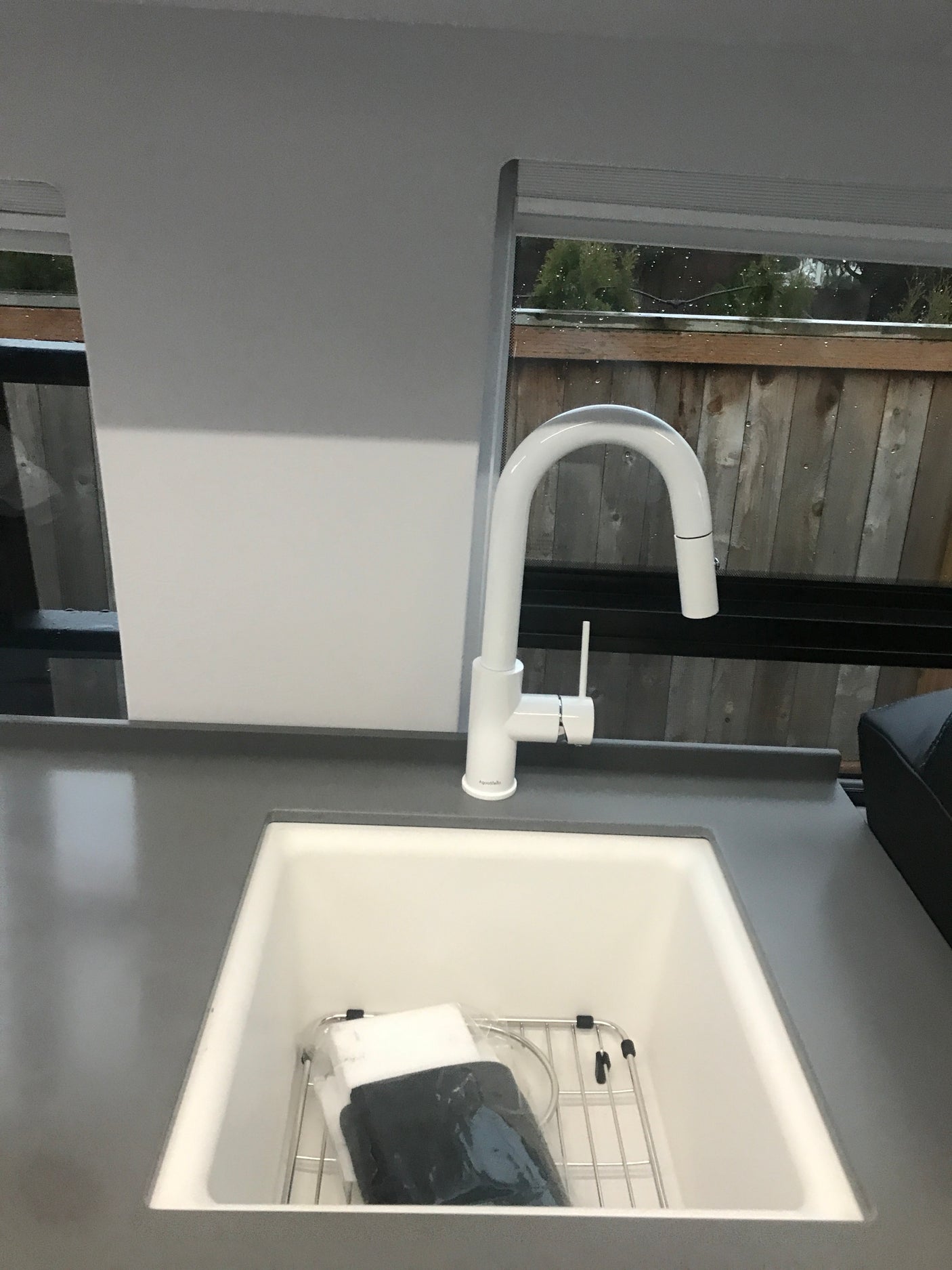 Modern white kitchen sink and pull-down faucet in an RV rental, with a view of greenery outside.